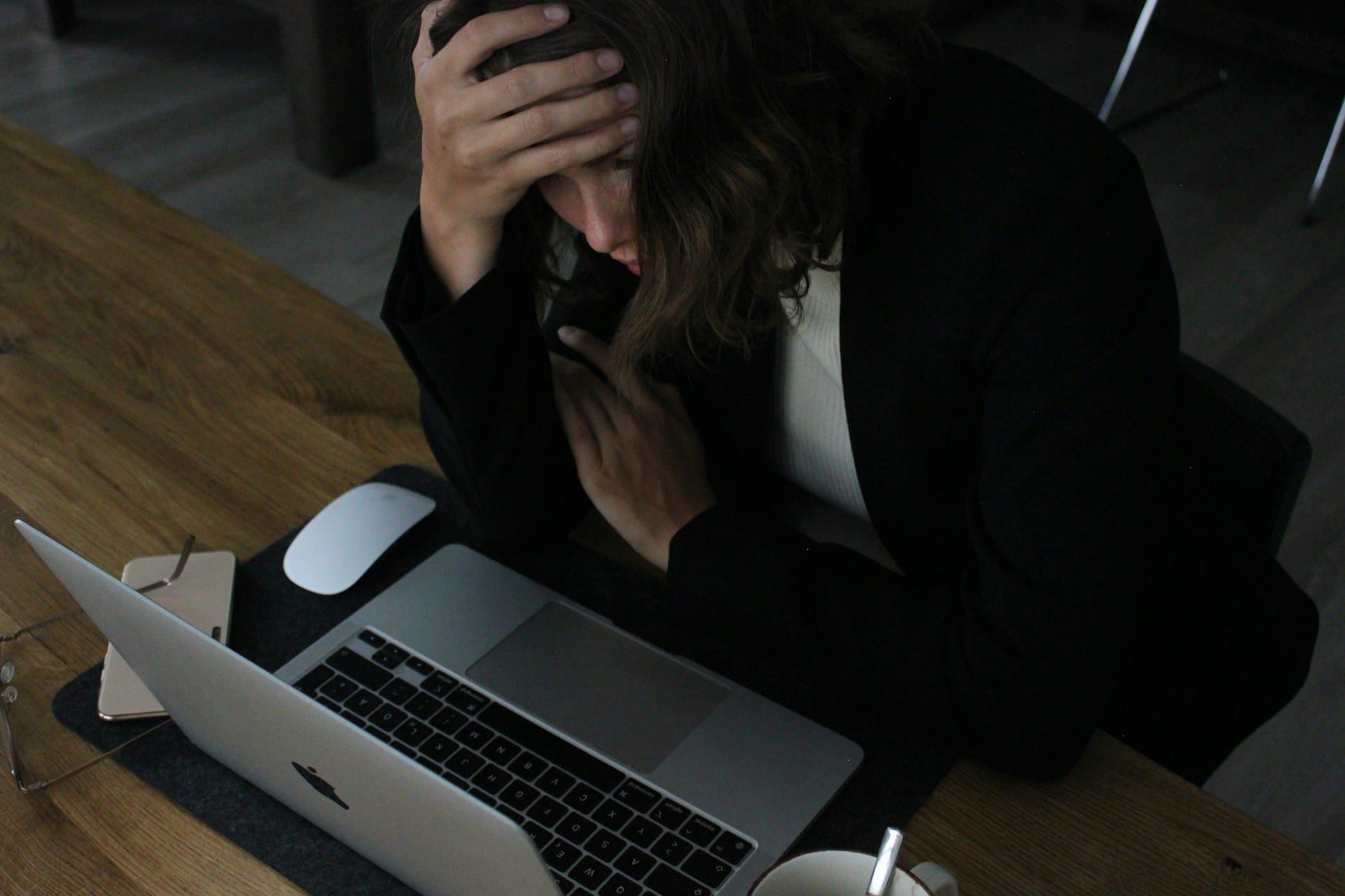 Person in distress at laptop showing signs of digital burnout and frustration while working at wooden desk.